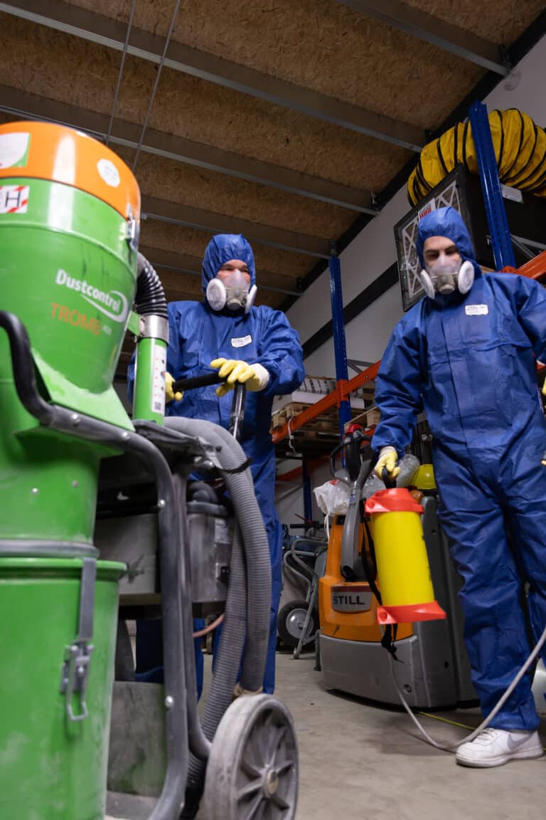 Fachkräfte in Schutzausrüstung mit Industriesauger der Staubklasse H und Sprühgerät